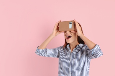 Young woman using cardboard virtual reality headset on color background. Space for text