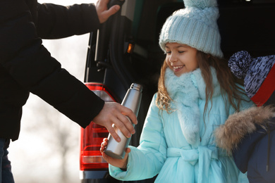 Photo of Father giving thermos to little daughter near car. Family trip