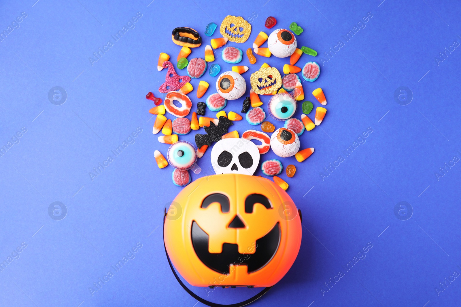 Photo of Halloween trick or treat bucket and different sweets on blue background, flat lay