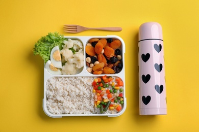 Photo of Thermos and lunch box with food on yellow background, flat lay