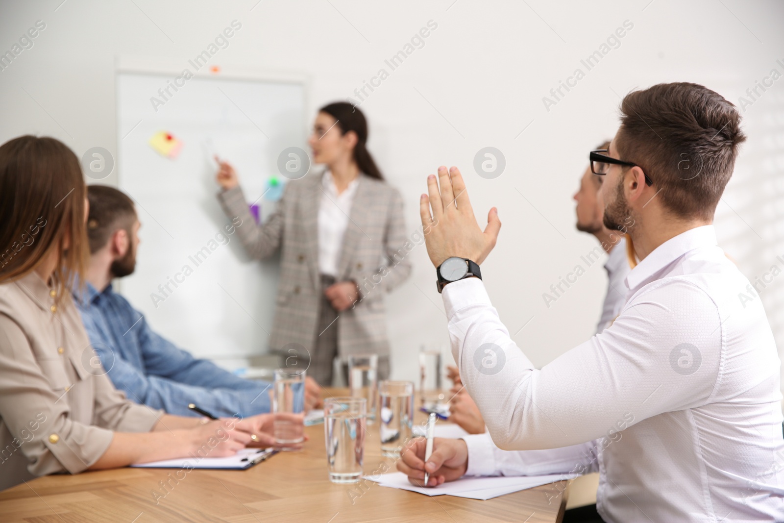 Photo of Young man raising hand to ask question at business training in conference room
