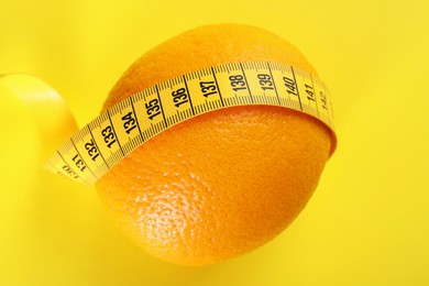 Photo of Cellulite problem. Orange with measuring tape on yellow background, top view