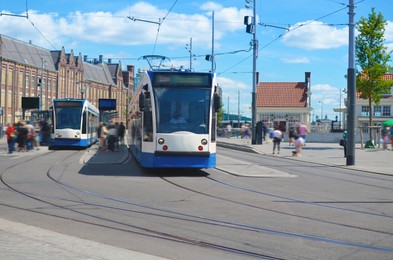 Photo of Modern streetcars and people at tram stop on sunny day