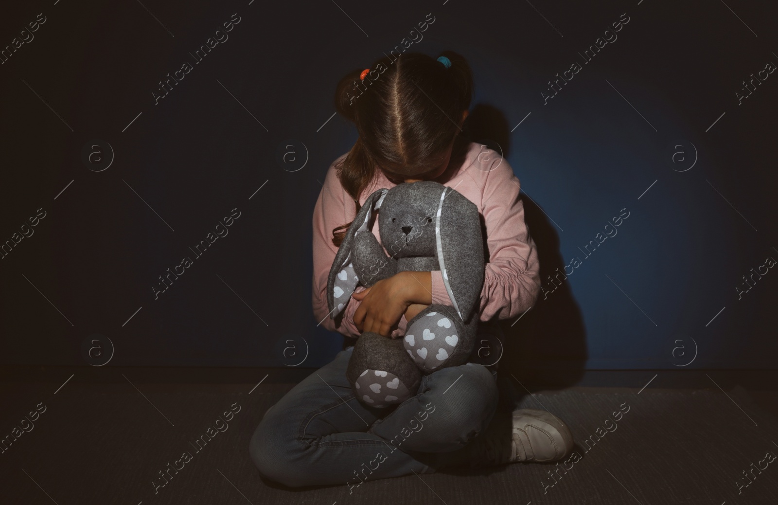 Photo of Scared little girl with toy near blue wall. Domestic violence concept