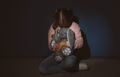 Photo of Scared little girl with toy near blue wall. Domestic violence concept