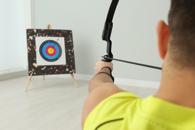 Photo of Man with bow and arrow aiming at archery target indoors, closeup