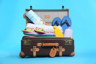 Open vintage suitcase with different beach objects packed for summer vacation on light blue background