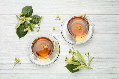 Cups of tea and linden blossom on white wooden table, flat lay