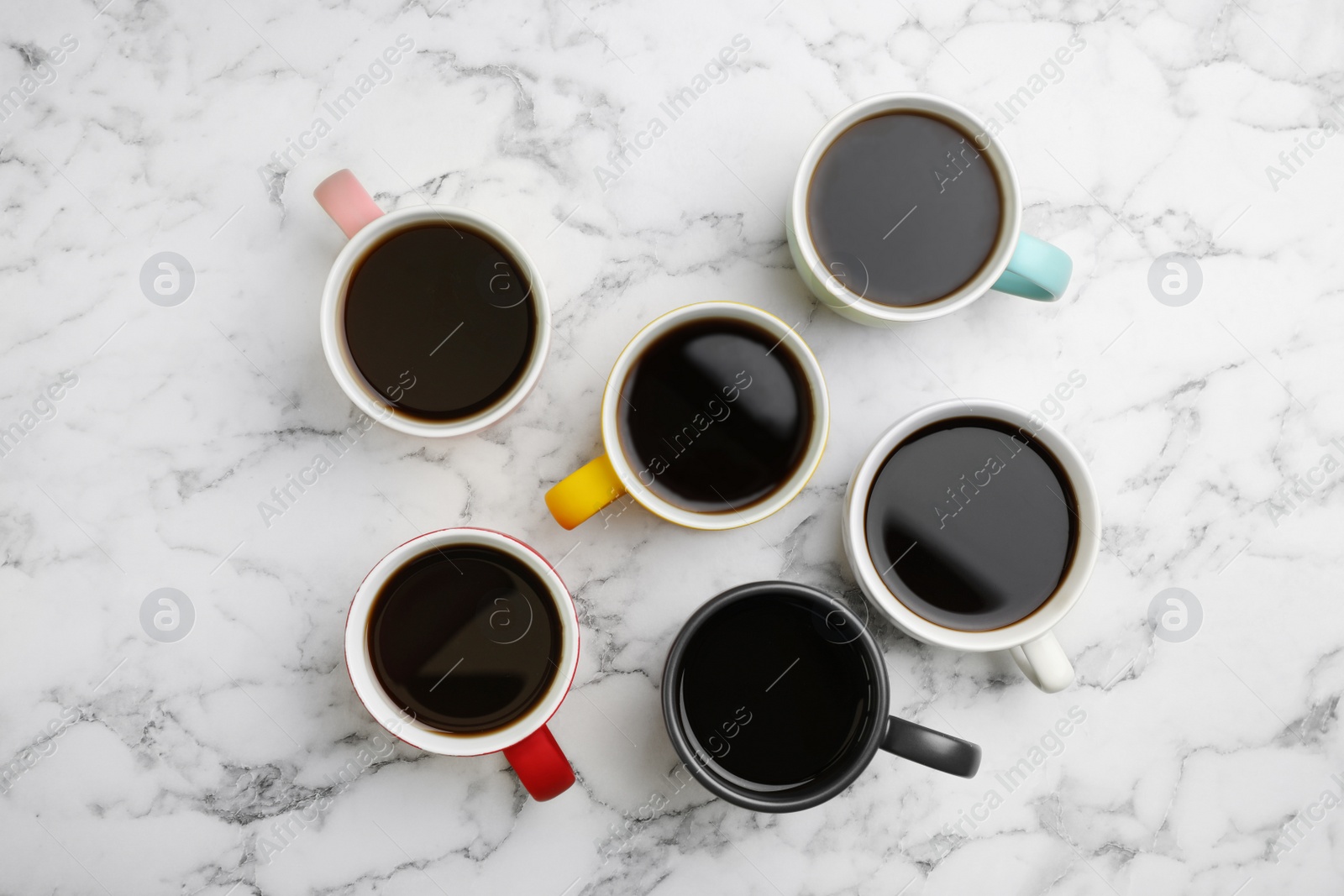 Photo of Many ceramic cups with hot aromatic coffee on marble background, flat lay