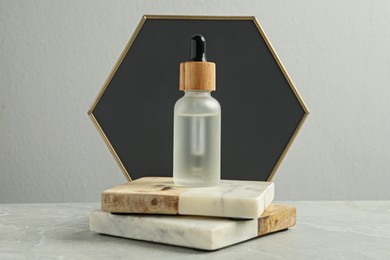 Photo of Bottle of face serum with marble boards on table against grey background