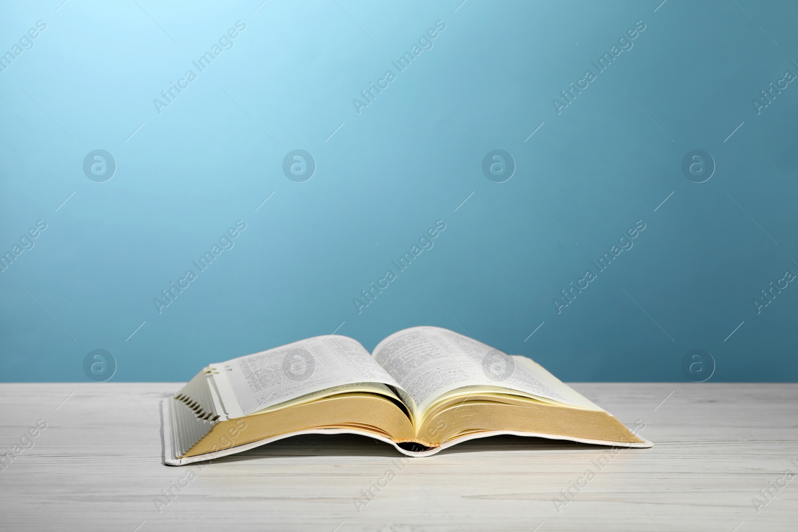 Photo of Open Bible on white wooden table against turquoise background. Christian religious book