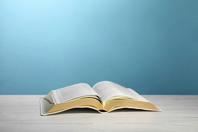 Open Bible on white wooden table against turquoise background. Christian religious book