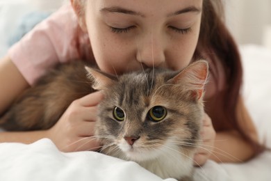 Photo of Cute little girl with cat lying on bed at home, closeup. First pet
