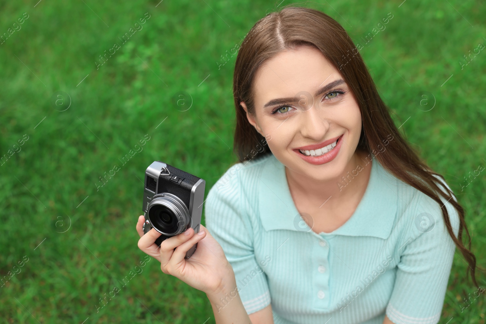 Photo of Young woman with camera on green grass outdoors, space for text. Interesting hobby