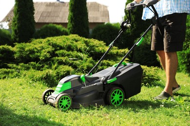 Photo of Man cutting grass with lawn mower in garden on sunny day, closeup