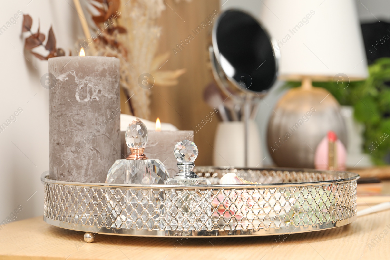 Photo of Perfumes and burning candles on wooden makeup table