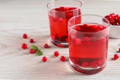 Tasty cranberry juice in glasses and fresh berries on white wooden table. Space for text