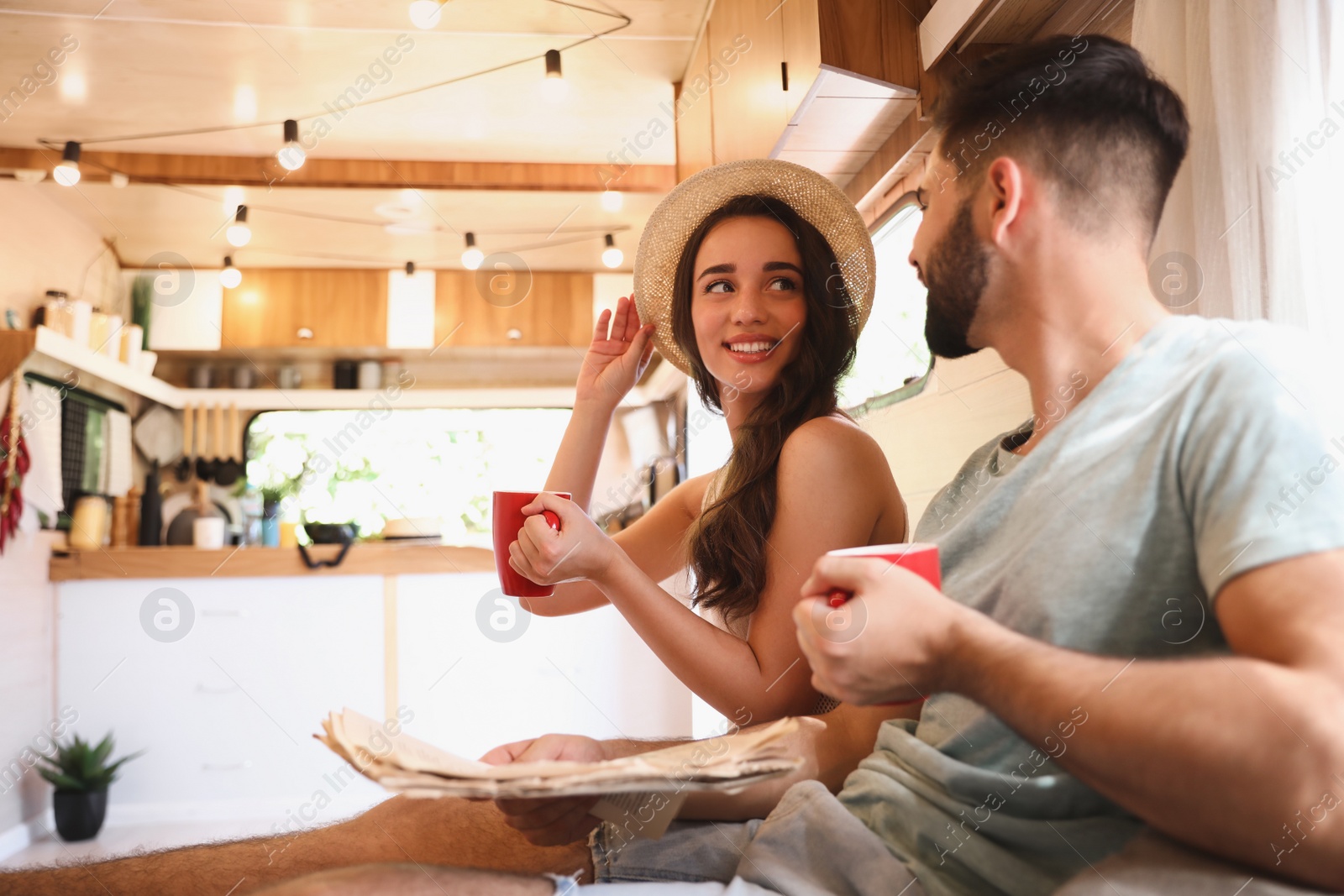 Photo of Happy young couple with cups and newspaper in trailer. Camping vacation