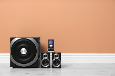 Photo of Modern powerful audio speaker system on floor near orange wall. Space for text