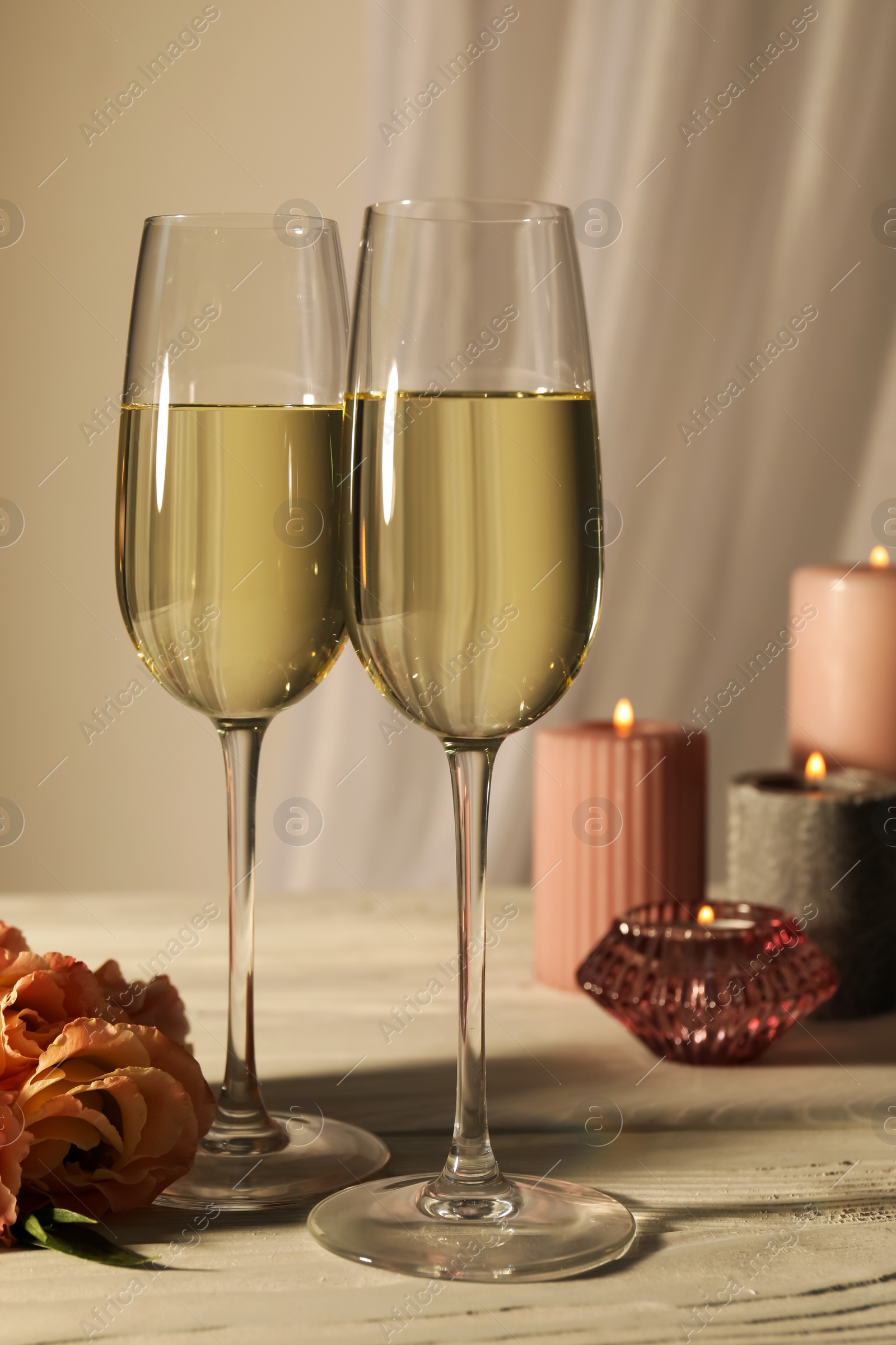 Photo of Glasses of sparkling wine, flowers and burning candles on white table