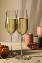 Glasses of sparkling wine, flowers and burning candles on white table