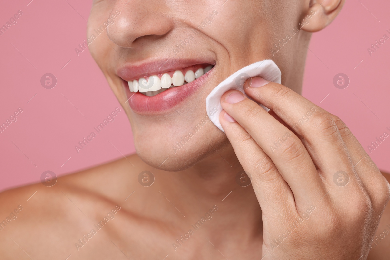 Photo of Man cleaning face with cotton pad on pink background, closeup
