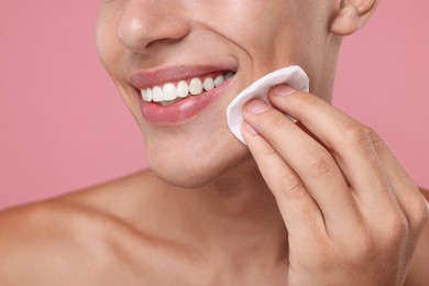 Photo of Man cleaning face with cotton pad on pink background, closeup