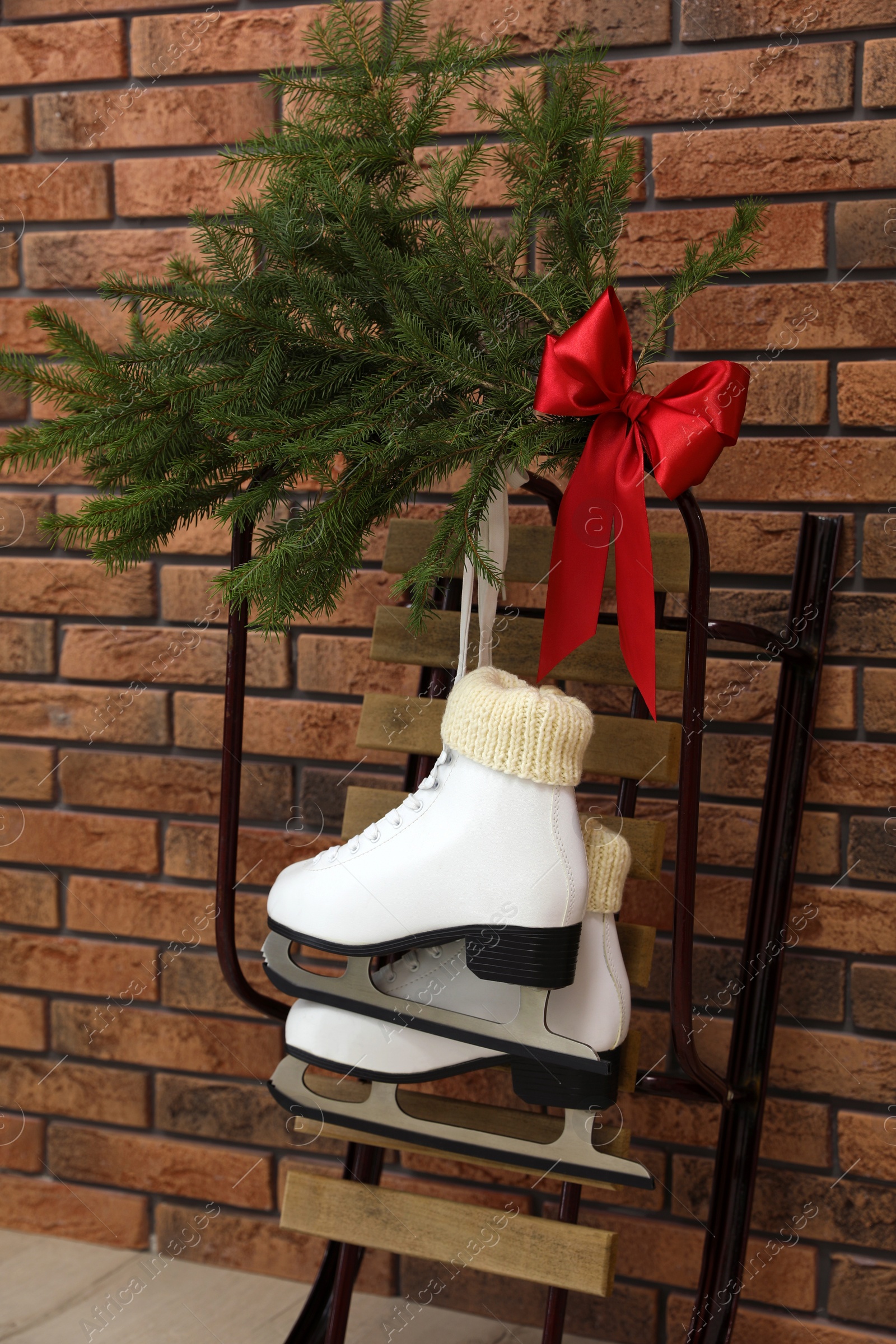 Photo of Sleigh with pair of ice skates and fir branches near brick wall indoors