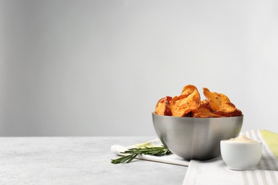 Photo of Bowl of sweet potato chips with sauce and rosemary on table against light background. Space for text
