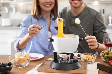 Photo of Happy couple enjoying fondue dinner at home, closeup