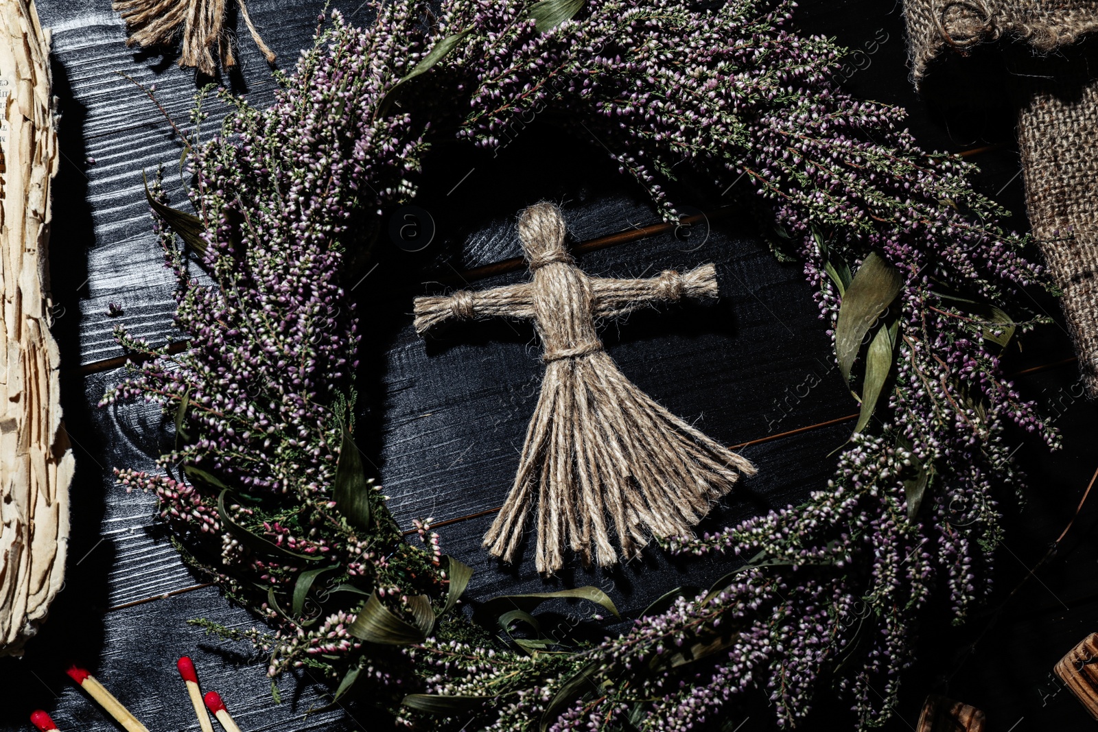 Photo of Female voodoo doll surrounded by ceremonial items on black wooden background, flat lay