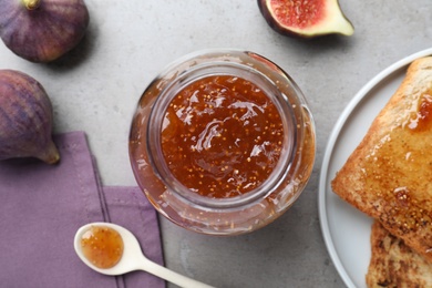 Photo of Delicious fig jam in glass jar on grey table, flat lay