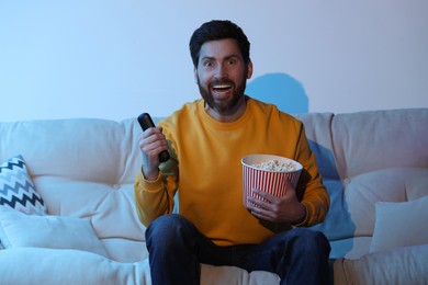 Photo of Surprised man watching TV with popcorn on sofa