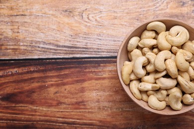 Photo of Tasty cashew nuts in bowl on wooden table, top view. Space for text