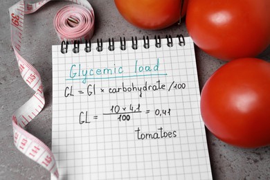 Notebook with calculated glycemic load for tomatoes, measuring tape and fresh vegetables on grey table, above view