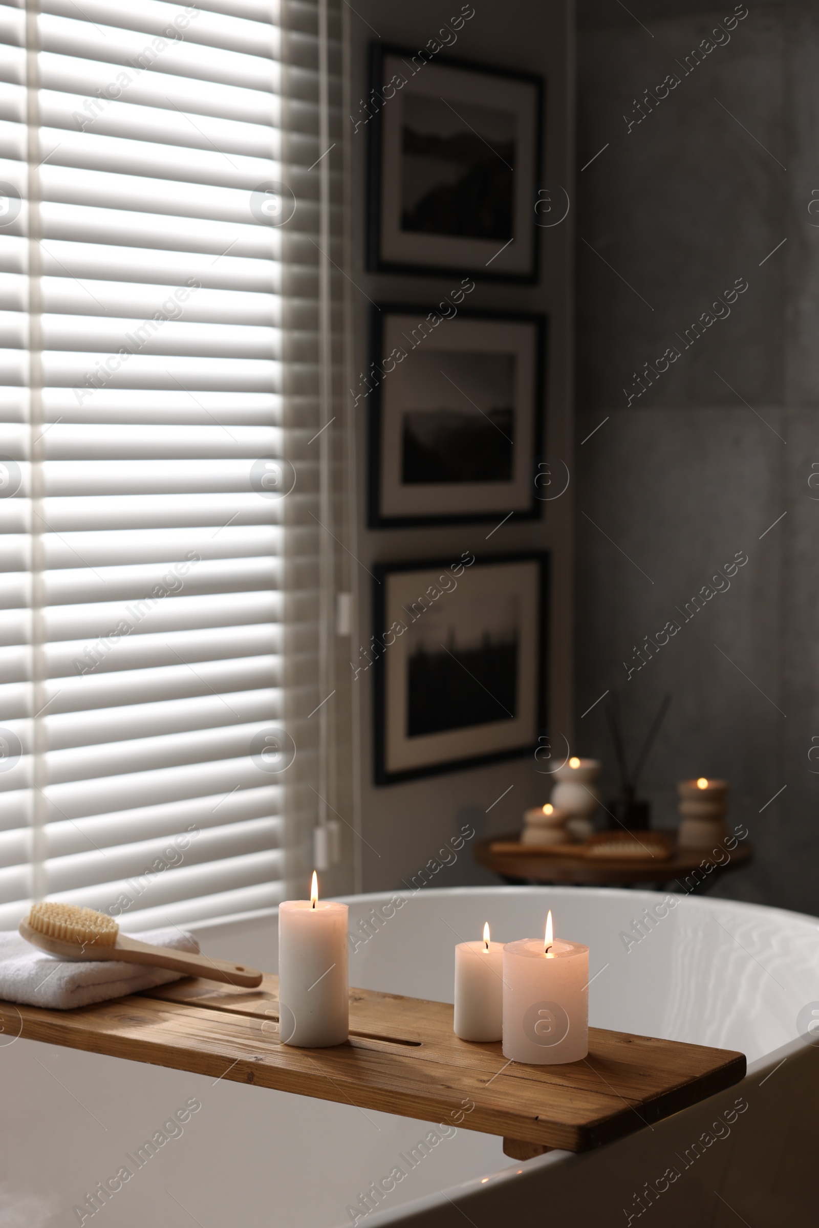 Photo of Wooden tray with burning candles, towel and brush on bathtub in bathroom