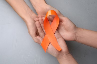 Couple holding orange ribbon on light grey background, top view. Multiple sclerosis awareness