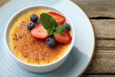 Photo of Delicious creme brulee with berries and mint in bowl on wooden table, above view