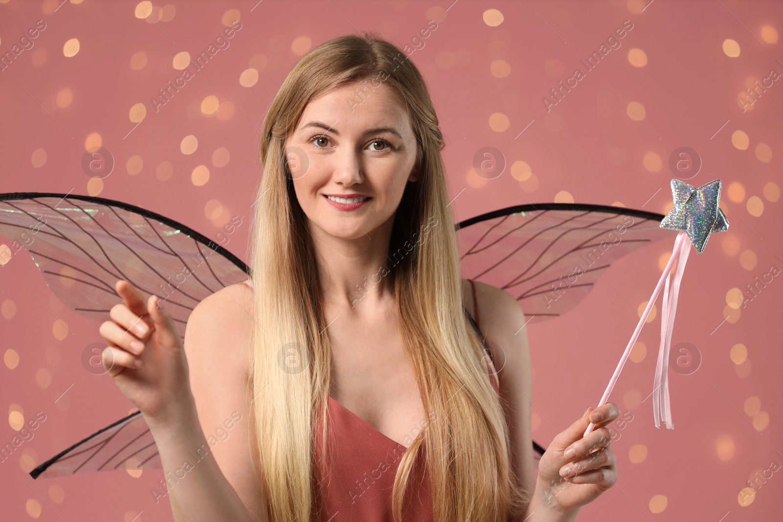 Photo of Beautiful girl in fairy costume with wings and magic wand on pink background