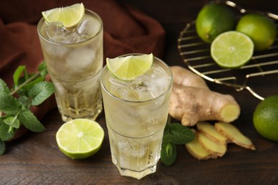 Photo of Glasses of tasty ginger ale with ice cubes and ingredients on wooden table, closeup