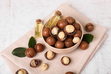 Photo of Bowl with organic Macadamia nuts and natural oil on white textured table