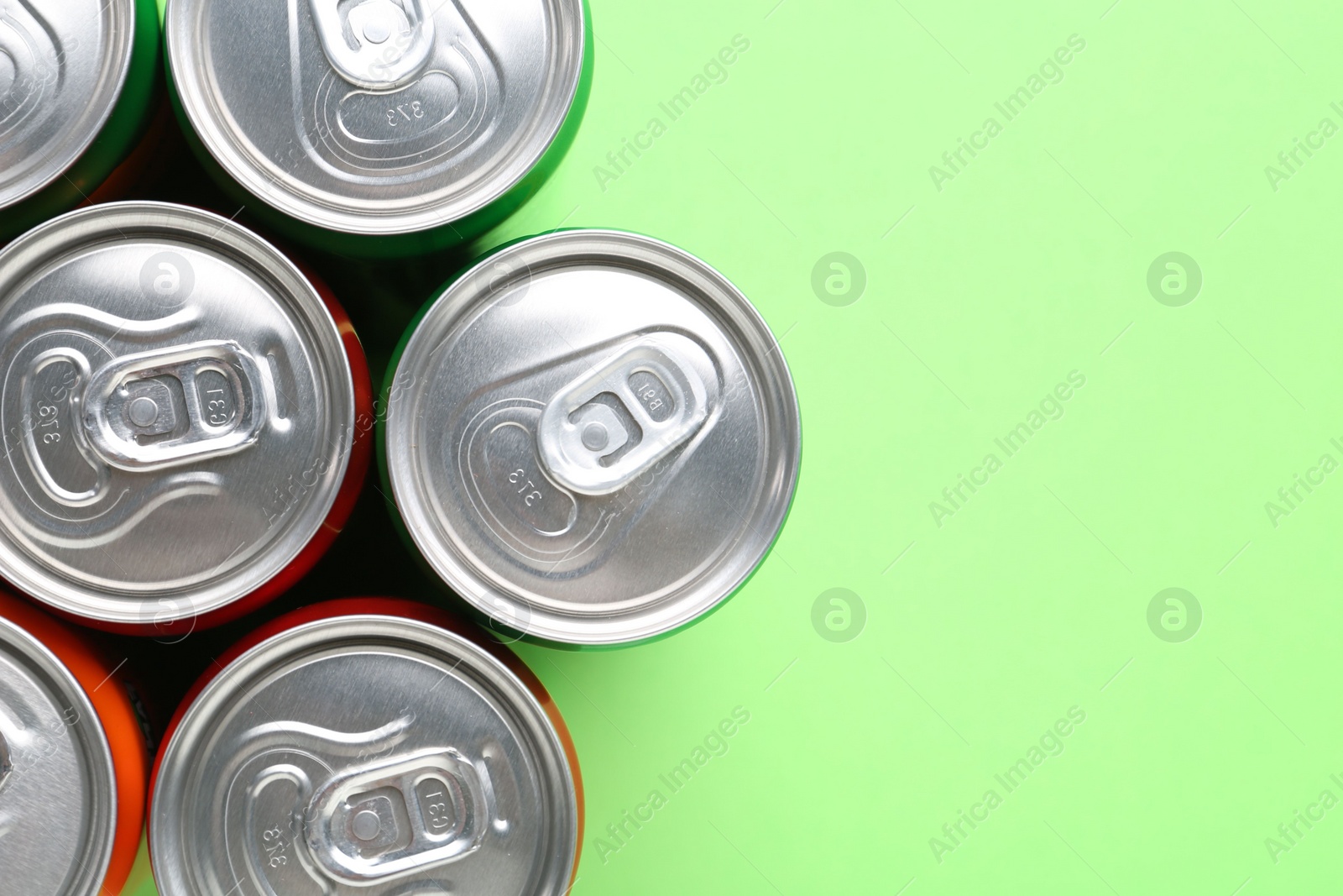 Photo of Energy drink in cans on light green background, top view. Space for text