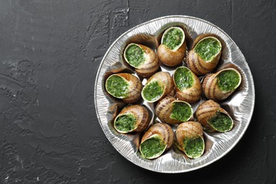 Photo of Delicious cooked snails on dark textured table, top view. Space for text