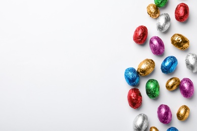 Photo of Chocolate eggs wrapped in colorful foil on white background, flat lay. Space for text