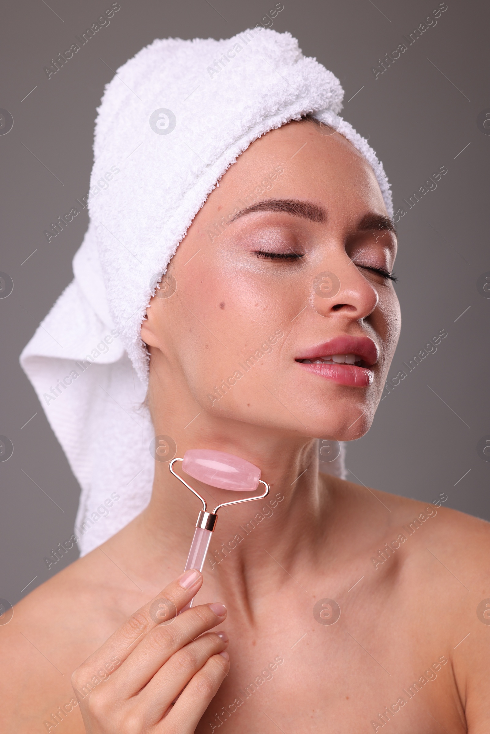 Photo of Young woman massaging her face with rose quartz roller on grey background