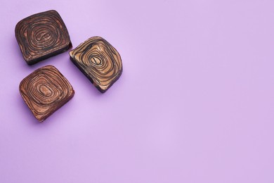 Tasty chocolate candies on violet background, flat lay. Space for text