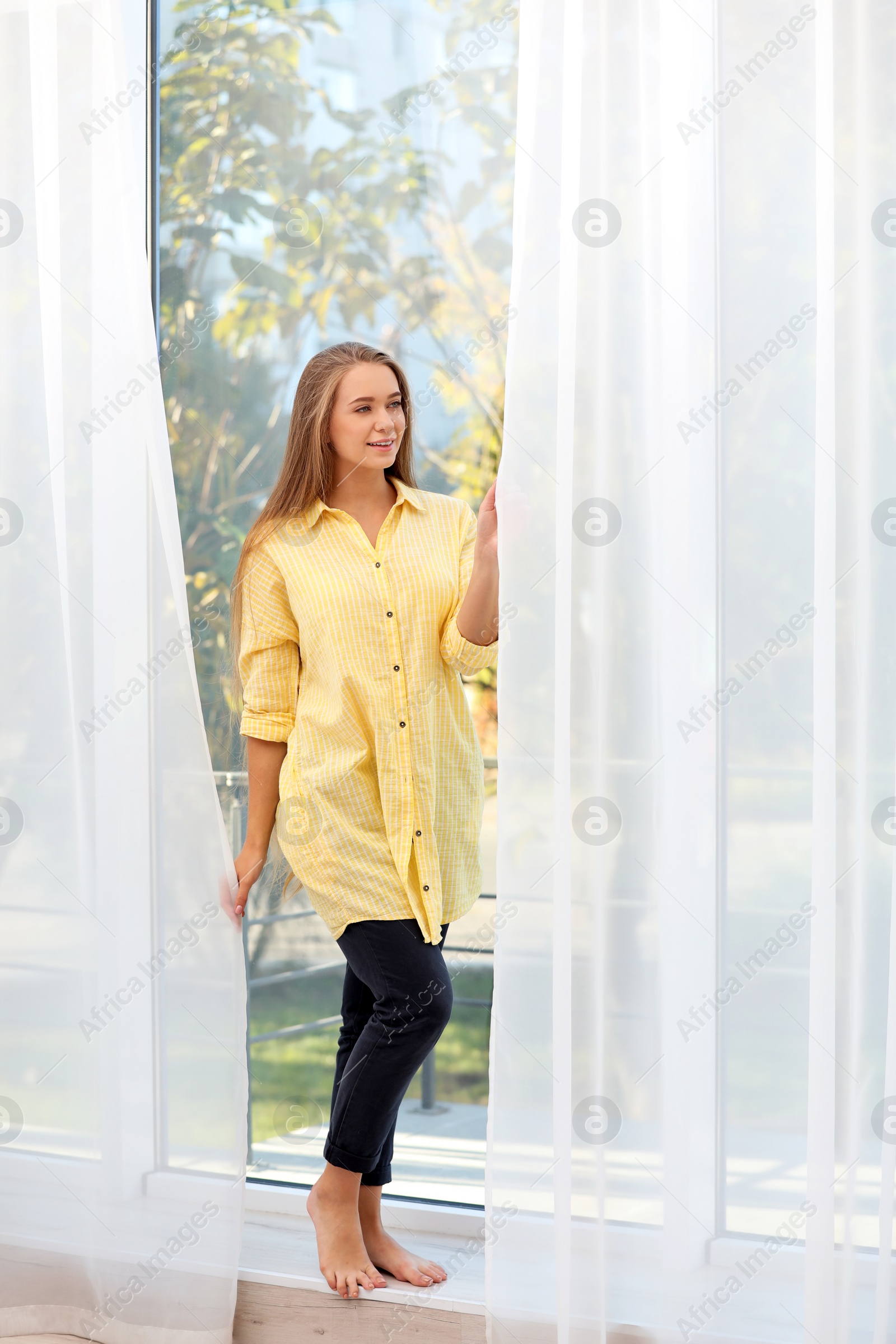 Photo of Young woman near window with open curtains at home