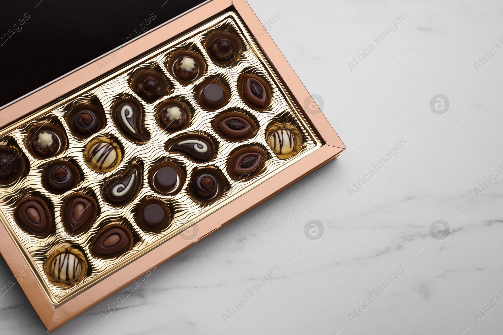 Photo of Box of delicious chocolate candies on white marble table, top view. Space for text