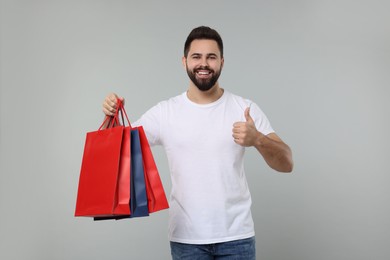 Photo of Happy man with many paper shopping bags showing thumb up on grey background