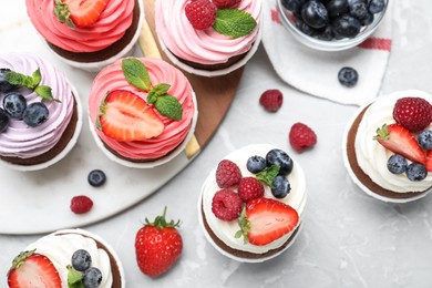Photo of Sweet cupcakes with fresh berries on light marble table, flat lay.